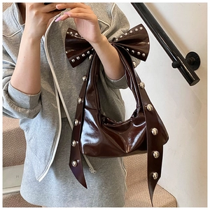 Detail of dark brown patent leather underarm bag with oversized bow and silver rivets
