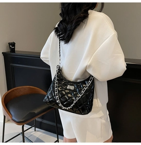 Detail of black quilted patent leather shoulder bag with silver chain and metal clasp