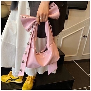 Detailed close-up of pink patent leather bag with silver rivets and bow accent