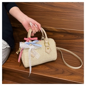 Détail du sac cylindre tissé beige avec nœud à carreaux bleu et bordure en dentelle