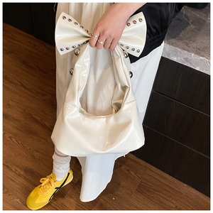Detail of white glossy rivet handbag with a large bow handle and silver metal accents