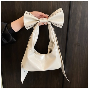 Close-up of cream white glossy leather bag with oversized studded bow and silver rivets