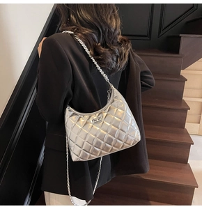 Silver quilted crescent bag with metallic finish and chain strap worn over a black blazer