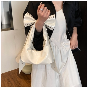 Macro detail of cream patent leather bag with large bow and silver rivet studs
