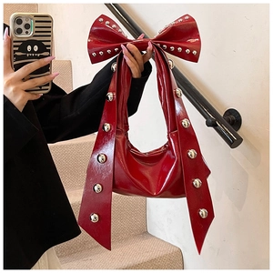 Detailed close-up of a red patent leather bag featuring a studded bow handle design