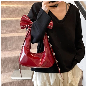Detail of dark red patent leather handbag featuring oversized bow and silver metal studs