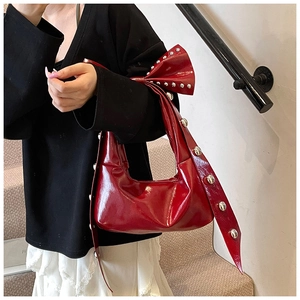 Close-up of red patent leather shoulder bag featuring bow detail and silver studs