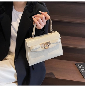 Creamy white crocodile texture Kelly style handbag with gold clasp held by a model