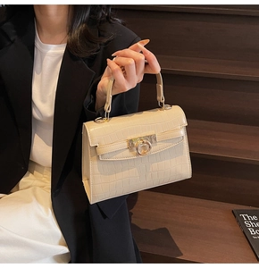 Close-up of cream faux crocodile leather handbag featuring elegant metal buckle and top handle