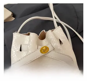 Detail of cream bucket bag featuring snake skin texture and gold twist lock closure