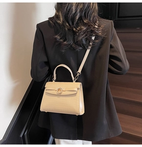 Detail of a creamy white crocodile pattern handbag with metal lock and thin shoulder strap