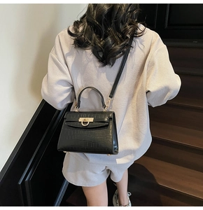 Detail of black faux crocodile texture handbag with gold metal lock on stairs