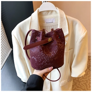 Detail of burgundy bucket bag with snake-skin texture and gold metallic twist lock