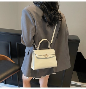 Detail of off-white crocodile embossed leather handbag with gold-tone ring buckle shown on model