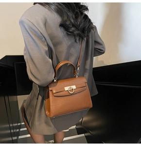 Close-up of brown crocodile texture handbag with gold ring clasp worn over a gray blazer
