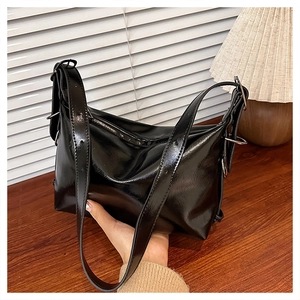 Close-up of glossy black leather tote bag with silver hardware on a wooden table