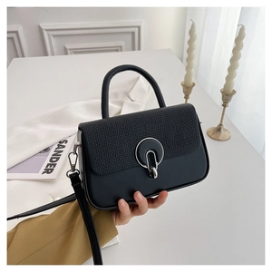 Detail of black crossbody bag featuring a textured woven flap and silver metal round buckle