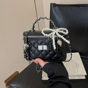 Detail of black quilted crossbody bag with pearl bow charm and silver chain strap