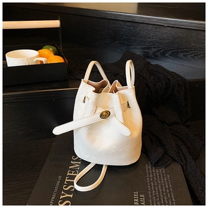 Detail of white crocodile pattern bucket bag with golden rotary lock on black background
