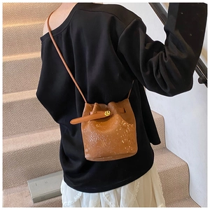 Detail of a brown croc-embossed bucket bag with a golden turn-lock and adjustable strap