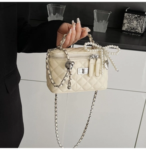 Detail of a quilted cream handbag with silver clasp, pearl bow, and chain strap