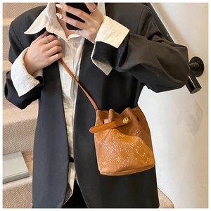 Close-up of brown snake skin bucket bag with metal lock worn by a model in a casual setting