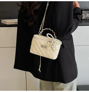Detail of beige quilted chain bag with pearl bow and heart charm worn with black blazer