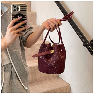 Detail of burgundy bucket bag with snake skin texture and golden twist lock closure