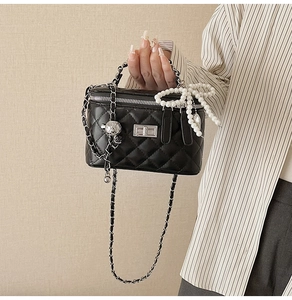 Detail of black quilted handbag featuring pearl bow and silver chain strap details