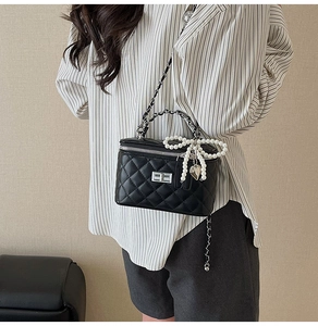 Detail of black quilted crossbody bag with silver chain, pearl bow and heart charm