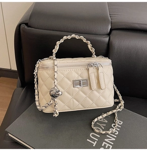 Detailed view of beige quilted chain handbag with silver twist lock and dual zip closure