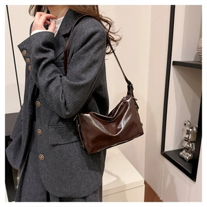 Detail of dark brown glossy tote bag with adjustable strap worn by model in minimalist setting