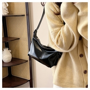 Detail of a glossy black half-moon underarm bag with silver zipper and adjustable strap