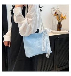 Detail of light blue canvas handbag featuring a white lace bow accent and soft texture