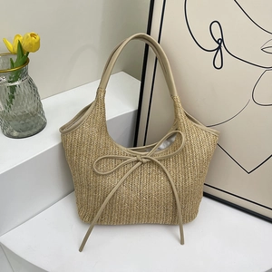 Beige straw tote bag with leather bow accent on a minimalist modern display stand