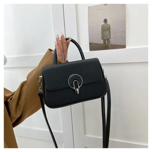 Detail of black crossbody bag featuring textured flap and silver ring buckle closure