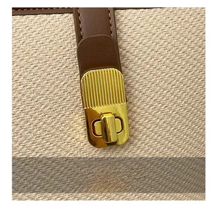 Close-up of golden twist lock and brown leather trim on beige canvas bucket bag