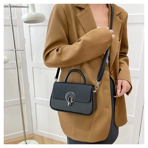 Detail of black crossbody bag featuring woven texture flap and round metal buckle