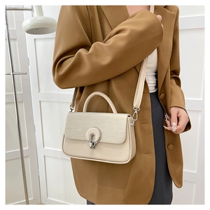 Detailed close-up of a beige crossbody bag featuring woven texture and a silver round buckle