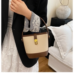 Detail of straw patchwork bucket bag with brown leather trim and gold metal buckle