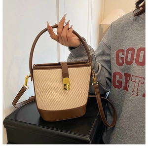 Detail of straw bucket bag with dark brown leather trim and golden metal clasp lock