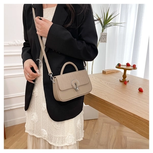 Detail of beige square bag showing leather stitching and silver metal round buckle