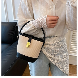 Close-up of contrast beige woven bucket bag with black leather handle and gold twist lock