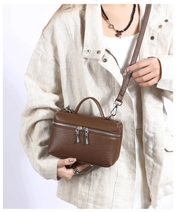 Detail of a brown lychee pattern leather handbag featuring dual silver zippers and handle