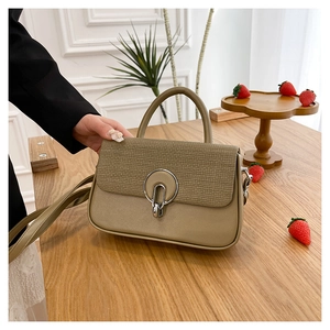 Close-up of khaki crossbody bag with woven texture lid and silver circular metal lock