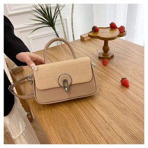 Detail of woven straw flap and metallic ring clasp on beige crossbody handbag