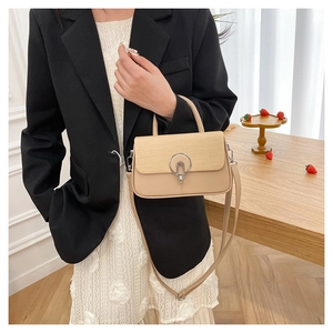 Detail shot of a beige shoulder bag with straw flap and silver metal lock on a wooden table