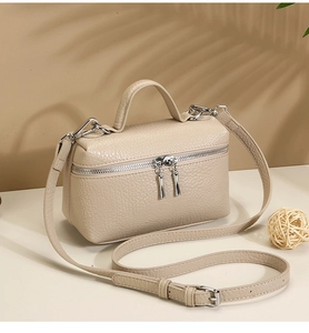 Close-up of beige lychee grain leather square bag with silver metal zippers and shadow