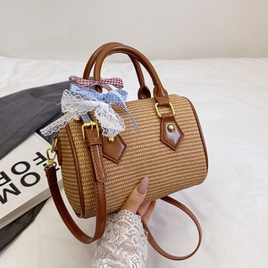 Sac à main cylindrique en paille avec garniture en cuir brun et nœud sur lit blanc