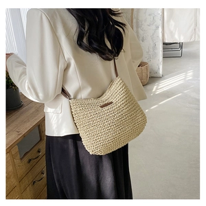 Detail of woven straw shoulder bag with leather straps on a model in natural light
